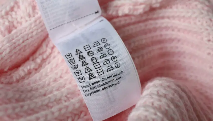 Pflegeetikett auf rosa Strickware: Waschsymbol 30 Grad mit 2 Strichen zeigt schonende Maschinenwäsche.