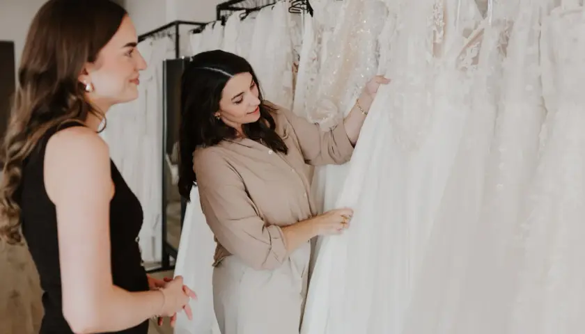 Eine Braut und eine Verkäuferin begutachten Brautkleid Schnitte in einem Brautmodengeschäft.