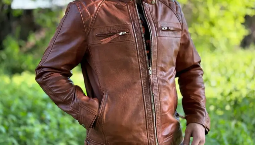 Mann in brauner Lederjacke mit Reißverschluss und gesteppten Schultern, vor grünem Hintergrund.