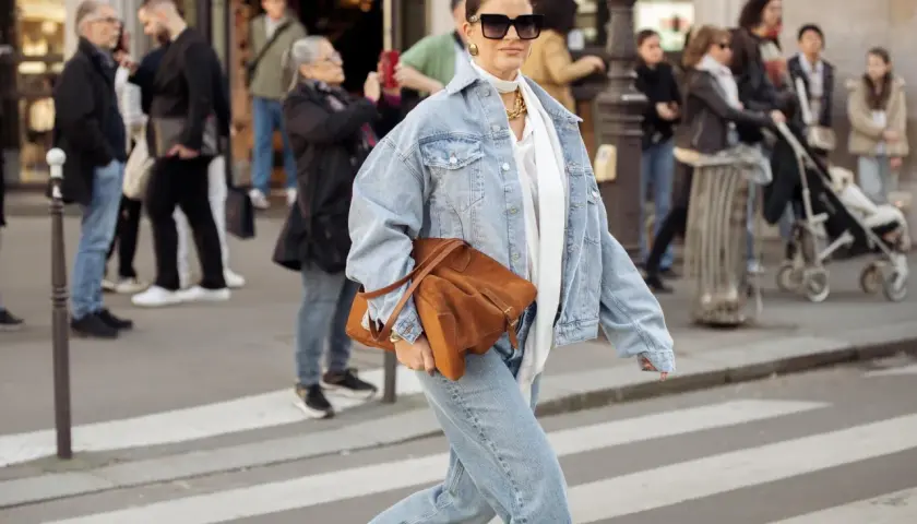 Frau in Jeansjacke und passender Hose, die eine braune Tasche trägt. Perfekt, welche Hose zu Jeansjacke passt!