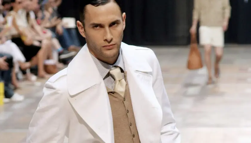 Ein Mann auf dem Laufsteg trägt einen weißen Trenchcoat über einem beigen Sakko, das er elegant kombiniert.