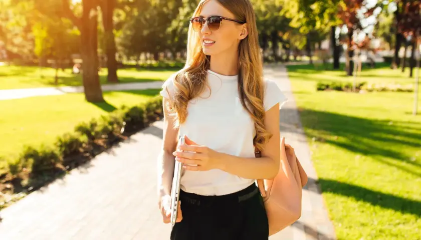 Junge Frau im Park, mit Laptop und Tasche, perfekt für business casual herren sommer.