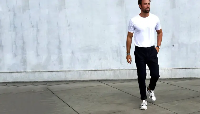 Mann in weißem T-Shirt und schwarzer Chino-Hose, dazu weiße Sneaker. Ein Beispiel, welche Schuhe zur Chino Hose Herren passen.