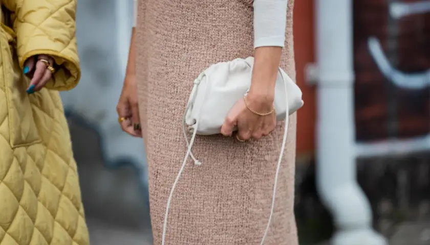 Ein gelber Steppmantel und ein Strickkleid mit weißem Langarmshirt darunter – ein perfekter layering look. Eine weiße Clutch rundet das Outfit ab.