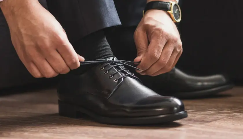 Mann schnürt schwarze Anzugschuhe. Die Wahl der richtigen Socken zum Anzug ist entscheidend für einen perfekten Look.