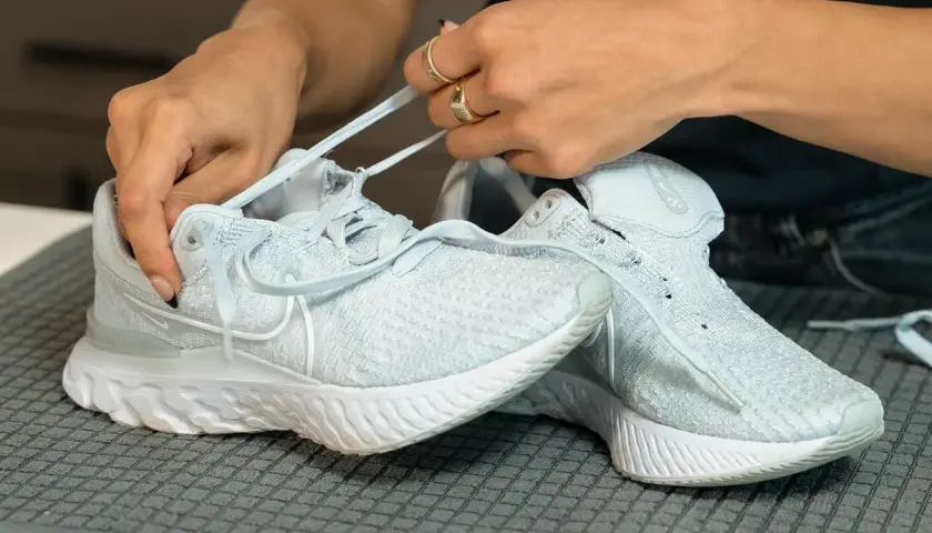 Hände binden Schnürsenkel an hellblauen Mesh-Schuhen, bereit für die Reinigung.