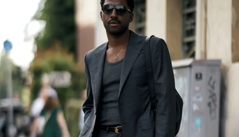 Ein Mann trägt einen eleganten Anzug mit Sneaker, dazu eine Kette und Sonnenbrille.