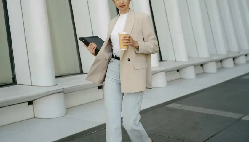 Frau im smart casual Look für Herren Winter, mit Blazer, Jeans und Kaffee.