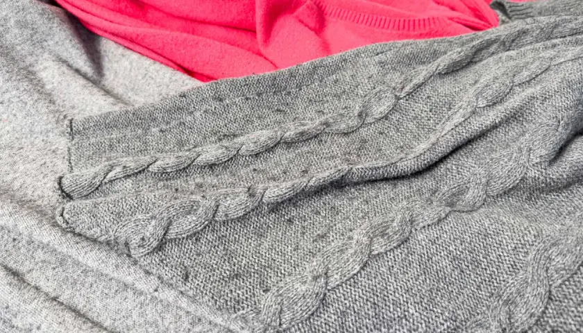 Grauer Strickpullover mit Zopfmuster, auf dem sich deutliches Pilling zeigt. Dies ist ein häufiger Reklamationsgrund bei Wollpullovern.
