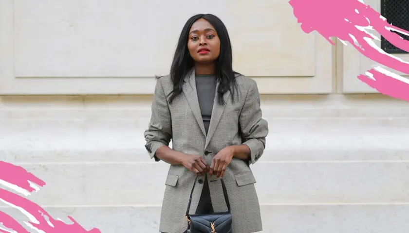 Eine Frau in einem karierten Blazer und dunklem Oberteil verkörpert smart business casual. Sie trägt eine schwarze Handtasche.