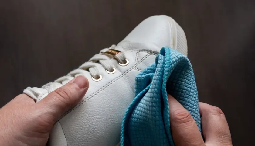 Hände polieren weiße Sneaker mit einem blauen Tuch. So werden die schuhe sauber machen und sehen wieder wie neu aus.