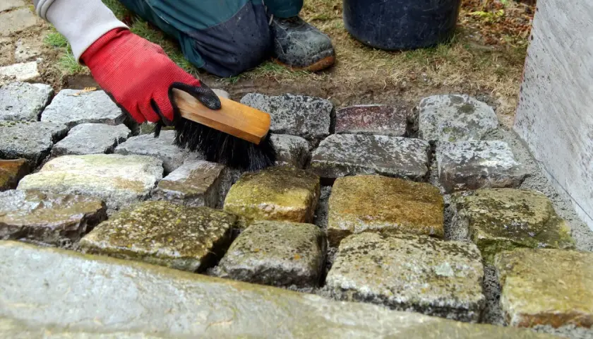 Mit roter Handschuh und Bürste werden eingetrocknete Fettflecken von Natursteinen entfernt.
