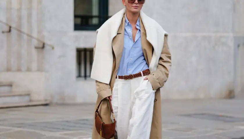 Frau im Trenchcoat, hellblauem Hemd und weißen Hosen, ein perfekter casual business look. Braune Tasche und Gürtel.