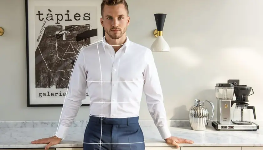 Mann mit weißem Hemd und blauer Hose, bereit, die Ärmel hochzukrempeln. Im Hintergrund ein Bild und eine Kaffeemaschine.