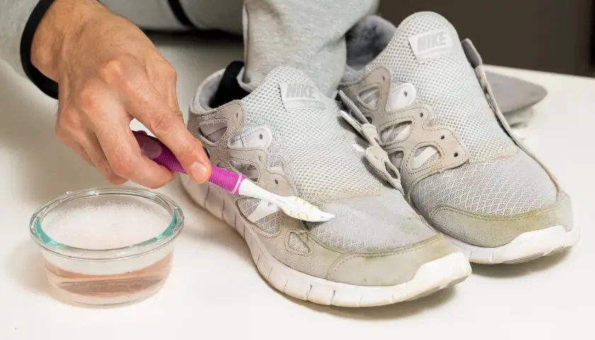 Schuhe reinigen: Mit einer Bürste und Seifenwasser werden Grasflecken von grauen Sneakern entfernt.
