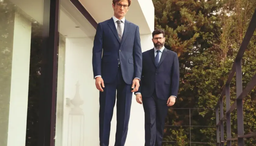 Zwei Männer in eleganten einreiher Anzügen stehen auf einer Holzterrasse vor einem modernen Gebäude.
