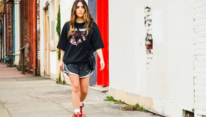 Frau stylt ein oversized T-Shirt mit Shorts und Sneakern, geht auf einem Bürgersteig.