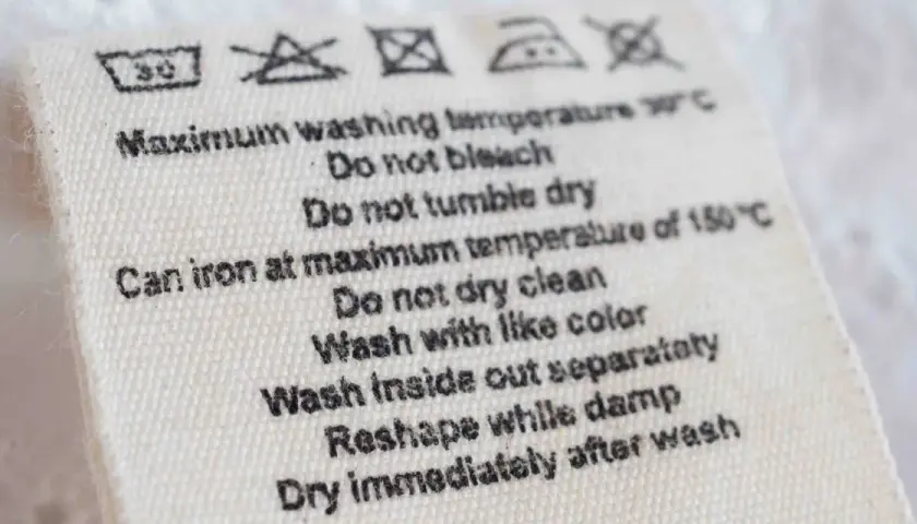 Pflegeetikett mit Symbolen und Anweisungen. Das Schonwaschgang Zeichen zeigt 30°C. Weitere Hinweise: nicht bleichen, nicht im Trockner trocknen, bügeln bei max. 150°C.