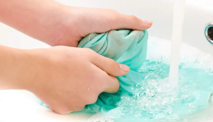 Hände waschen ein türkises Tuch in der Spüle, um Fettspritzer zu entfernen.