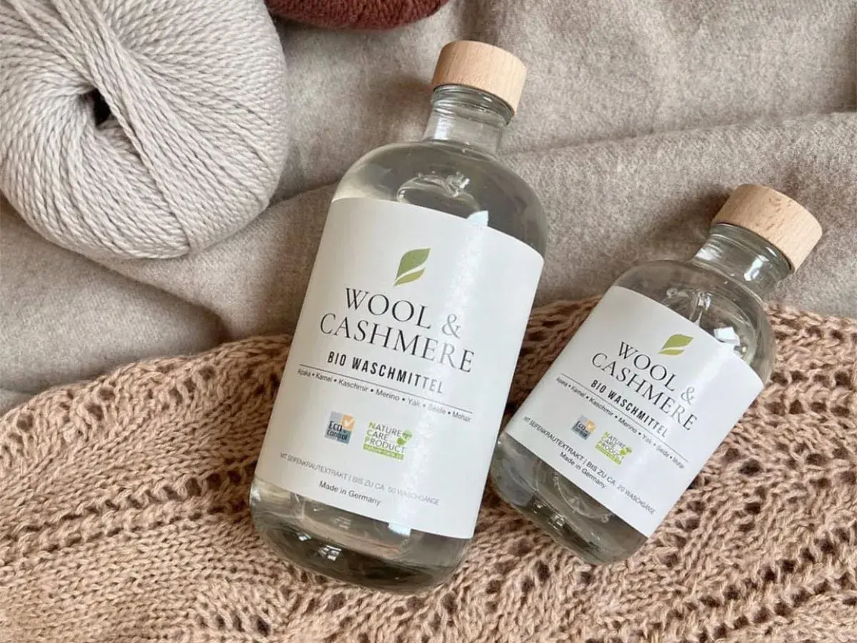 Zwei Flaschen "Wool & Cashmere" Bio-Waschmittel neben Garnknäueln und Strickwaren. Perfekt für die sanfte **Wolle waschen mit Shampoo**.