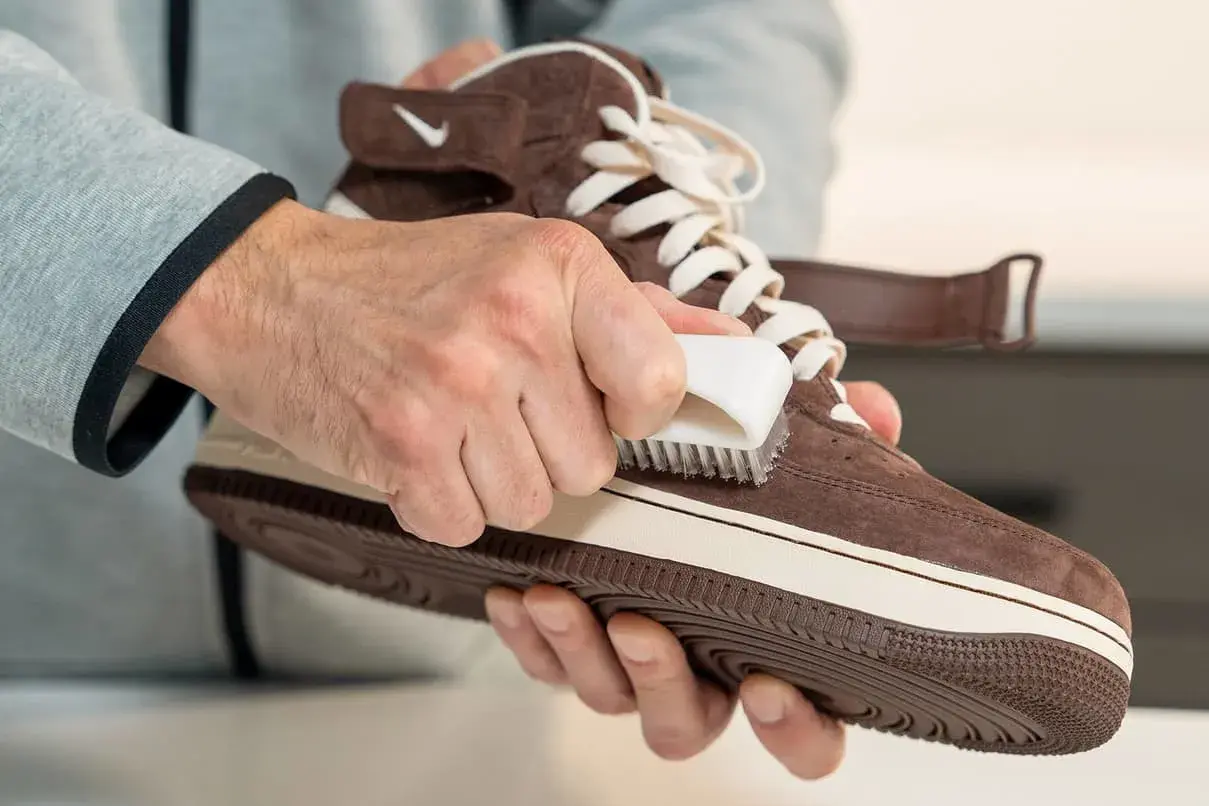 Hände pflegen braune Lederschuhe mit einer Bürste.