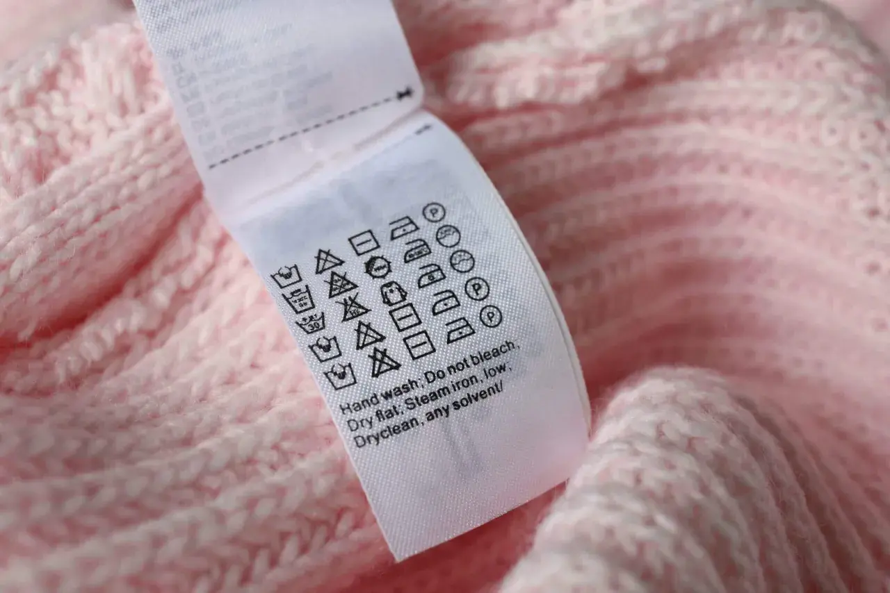 Pflegeetikett auf rosa Strickware: Waschsymbol 30 Grad mit 2 Strichen zeigt schonende Maschinenwäsche.