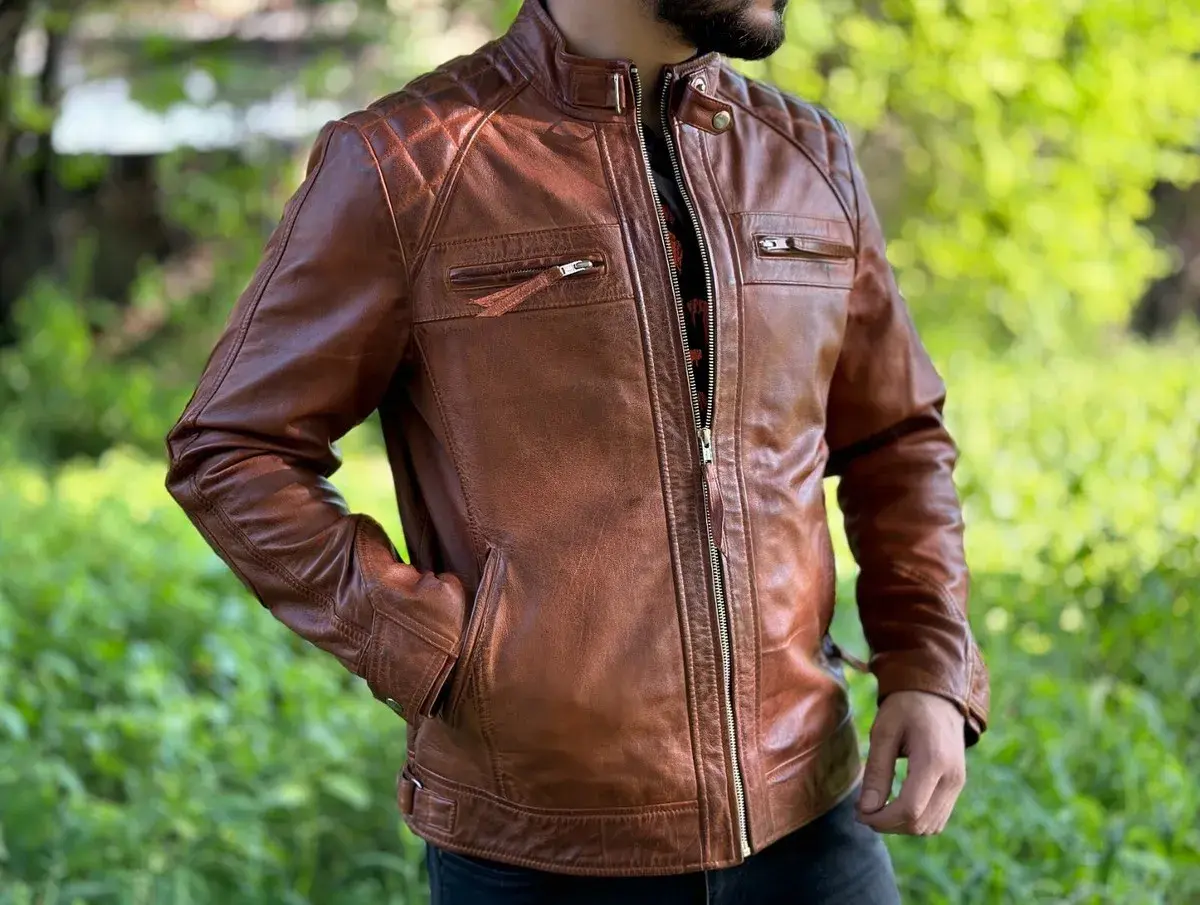 Mann in brauner Lederjacke mit Reißverschluss und gesteppten Schultern, vor grünem Hintergrund.