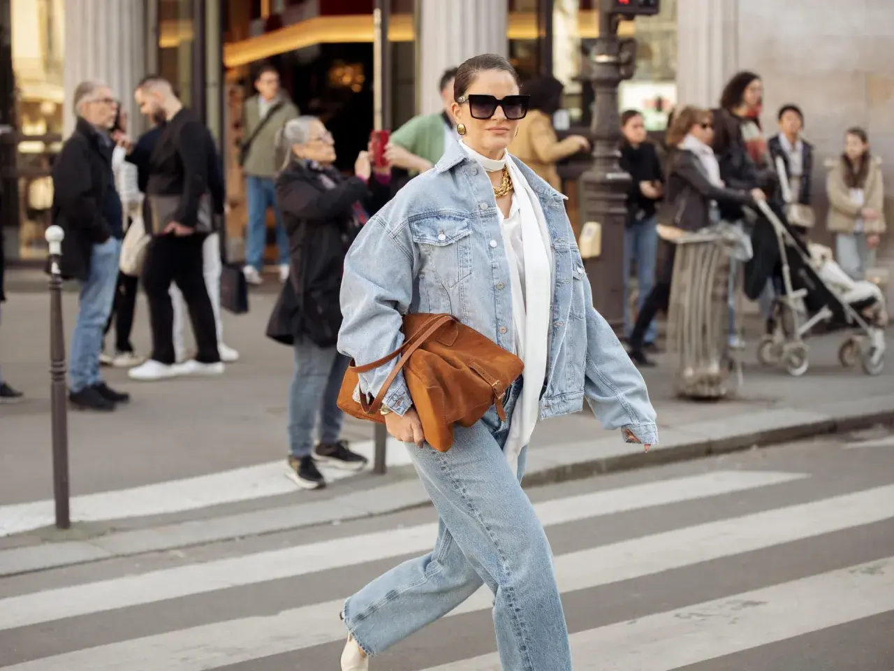 Frau in Jeansjacke und passender Hose, die eine braune Tasche trägt. Perfekt, welche Hose zu Jeansjacke passt!