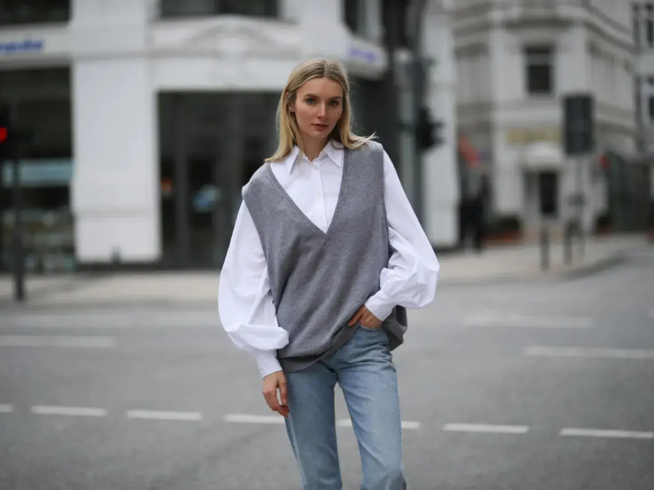 Eine Frau in einem weißen Hemd und Jeans trägt einen grauen Strick-Pullunder. So kann man Pullunder Damen kombinieren für einen lässigen Look.