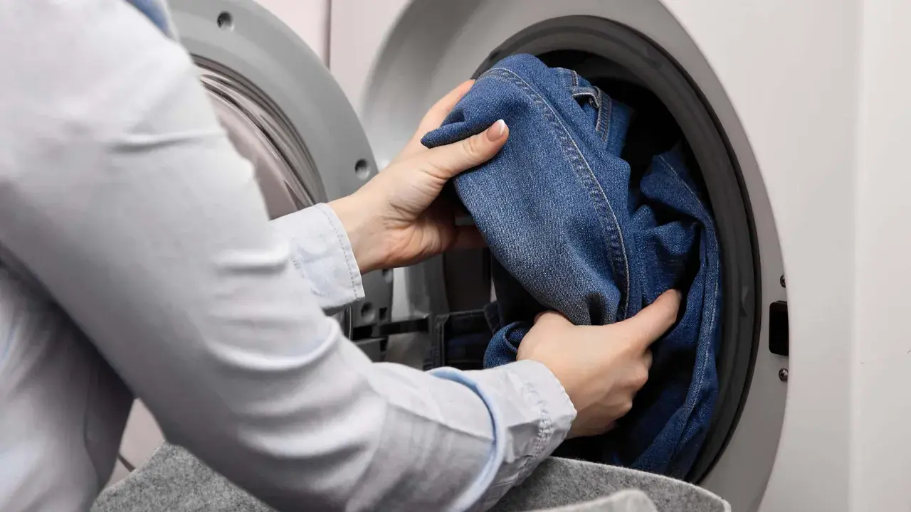 Hände legen Jeans in die Waschmaschine, um sie mit anderen Kleidungsstücken zu waschen.