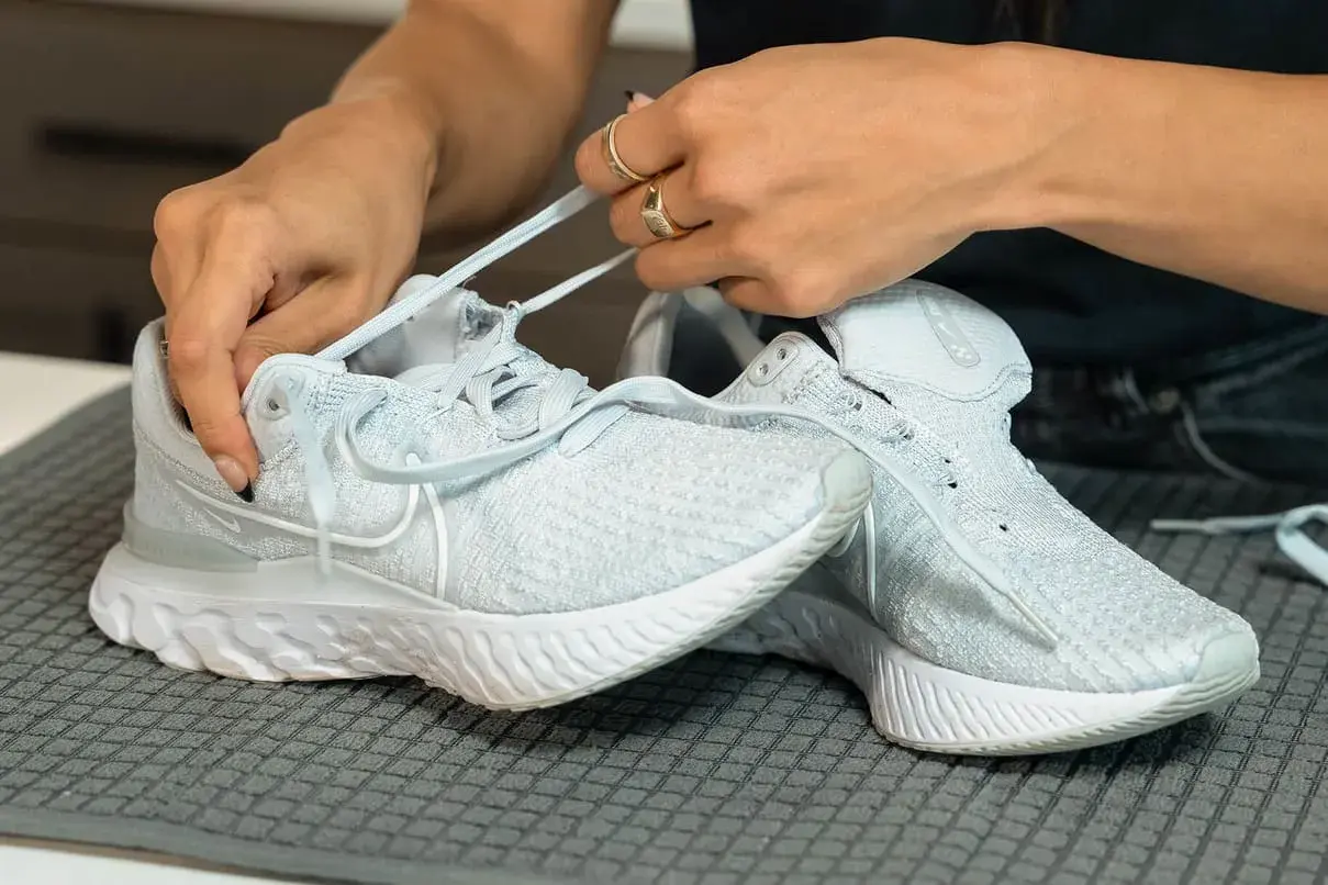 Hände binden Schnürsenkel an hellblauen Mesh-Schuhen, bereit für die Reinigung.