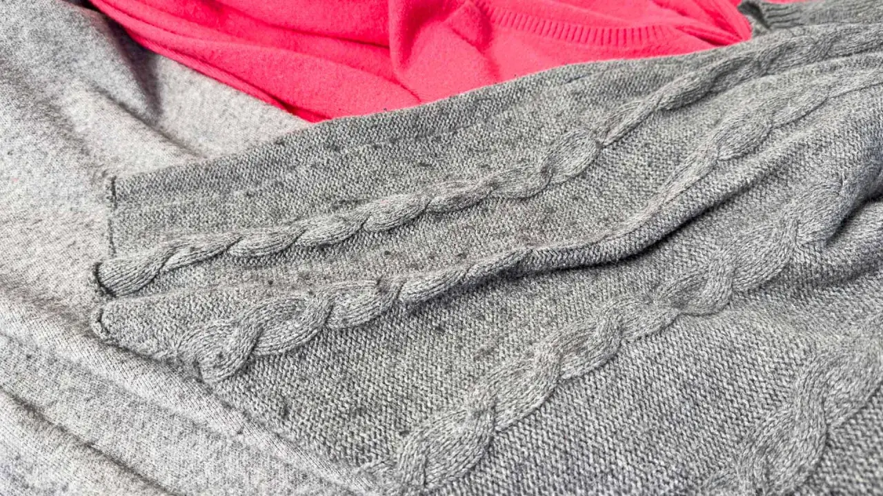 Grauer Strickpullover mit Zopfmuster, auf dem sich deutliches Pilling zeigt. Dies ist ein häufiger Reklamationsgrund bei Wollpullovern.