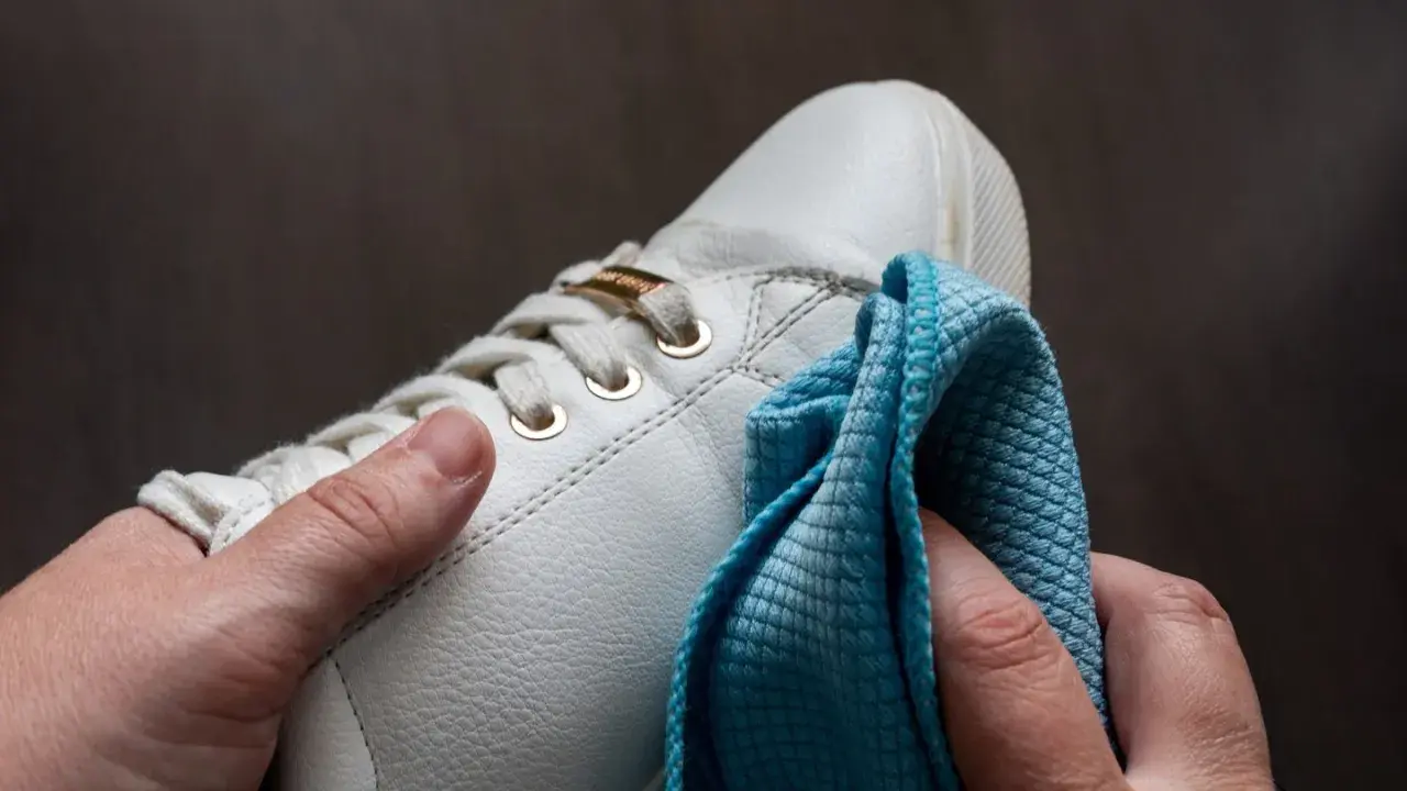 Hände polieren weiße Sneaker mit einem blauen Tuch. So werden die schuhe sauber machen und sehen wieder wie neu aus.