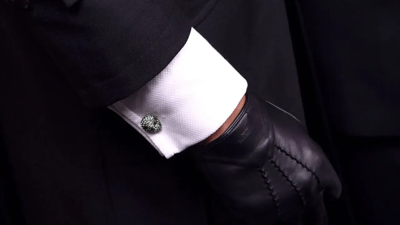 Elegante Manschettenknöpfe zieren das weiße Hemd unter einem schwarzen Anzug. Sie sind kleine Schmuckstücke, die zeigen, was sind Manschetten.
