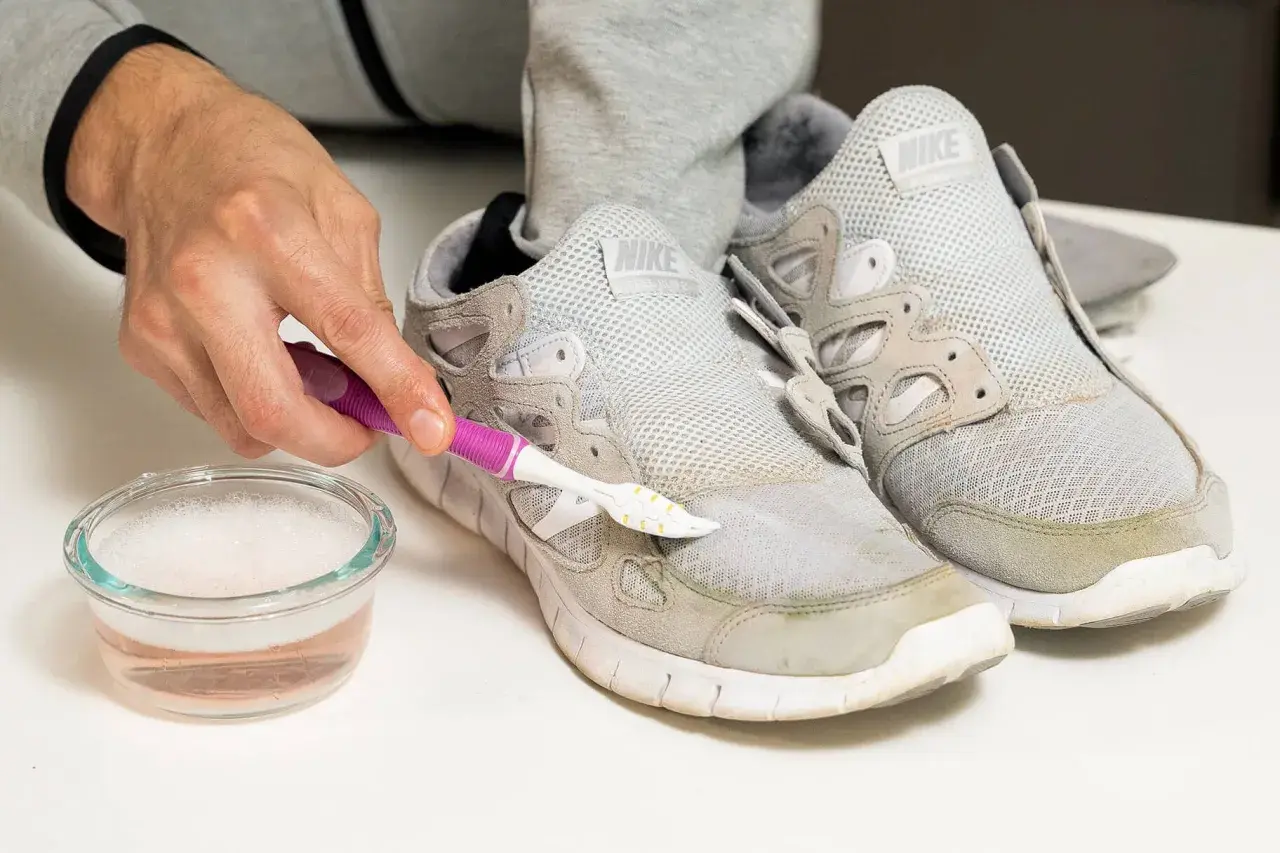 Schuhe reinigen: Mit einer Bürste und Seifenwasser werden Grasflecken von grauen Sneakern entfernt.