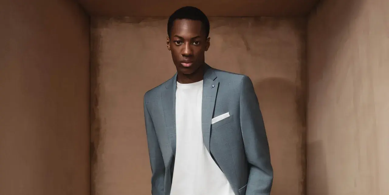 Junger Mann im grauen Anzug mit weißem T-Shirt und Einstecktuch. So trägt man einen Anzug richtig.