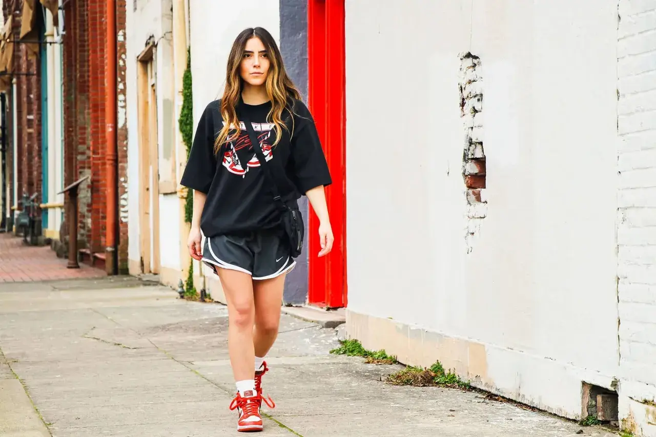 Frau stylt ein oversized T-Shirt mit Shorts und Sneakern, geht auf einem Bürgersteig.
