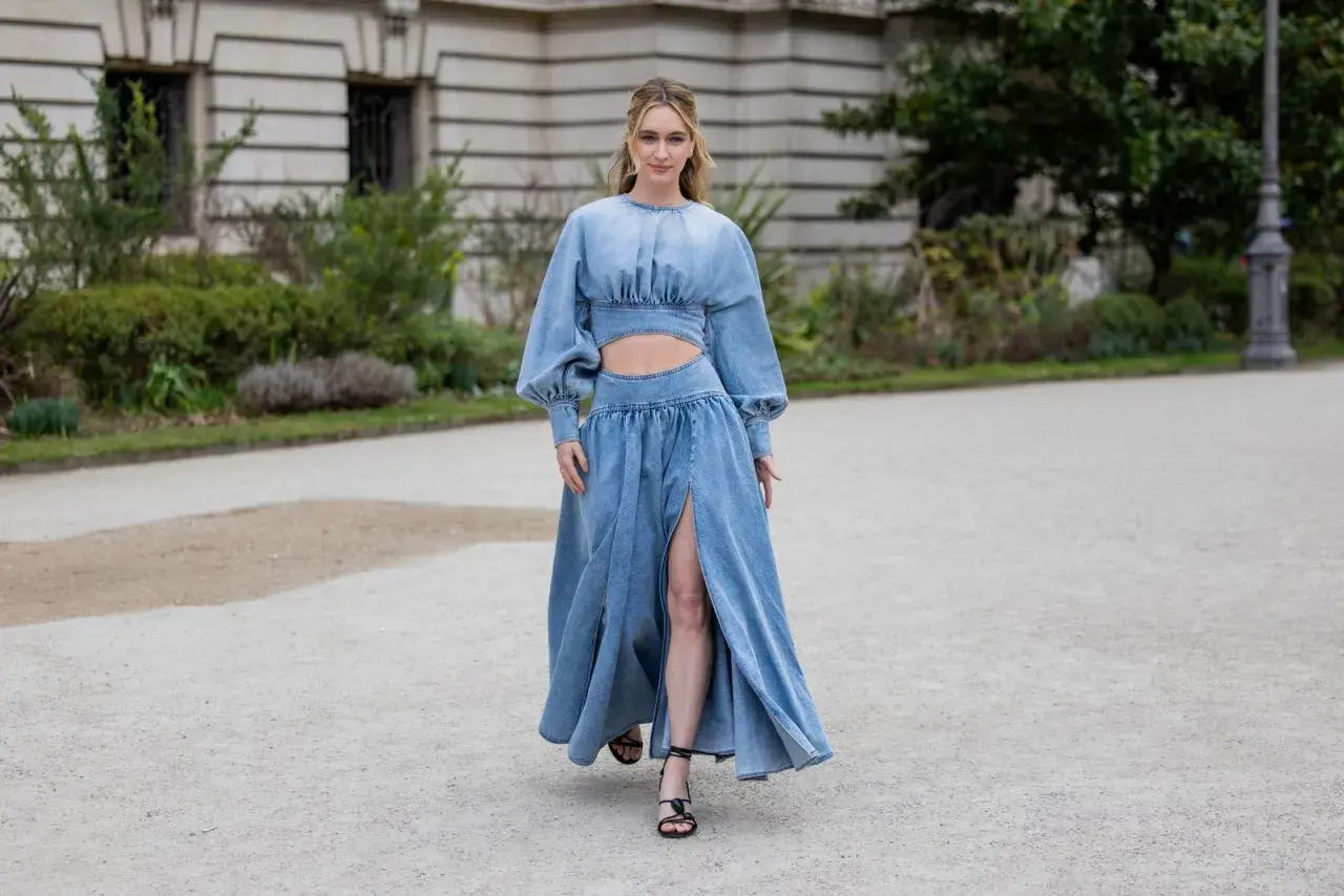 Frau in einem langen Jeanskleid mit Cut-outs und Puffärmeln, dazu schwarze Riemchensandalen. Die perfekte Inspiration, welche Schuhe zum Jeanskleid passen.