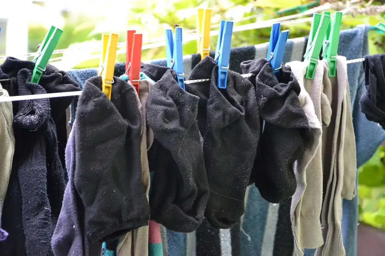 Schwarze Socken und andere Kleidungsst&uuml;cke trocknen an einer W&auml;scheleine. Die W&auml;sche wird mit bunten Klammern gehalten.