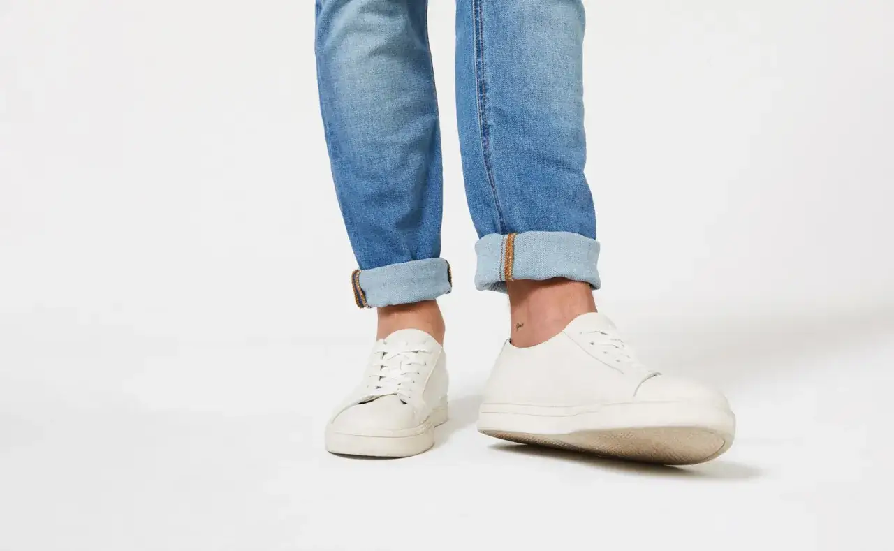 Person krempelt die hose nach innen und trägt weiße Sneaker. Der lässige Look ist perfekt für den Sommer.