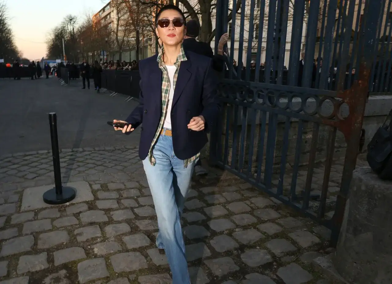 Eine Frau zeigt, wie man jeans elegant kombinieren damen kann: mit Blazer, kariertem Hemd und Sonnenbrille.