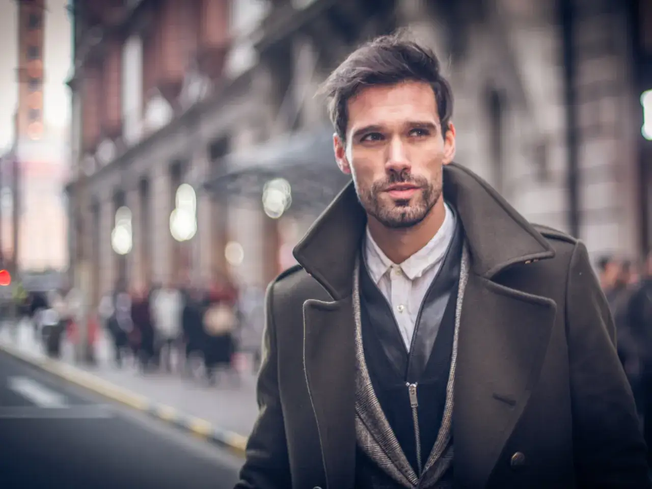 Ein Mann im eleganten Trenchcoat Herren Style, mit Bart und dunklem Haar, blickt nachdenklich in die Ferne.