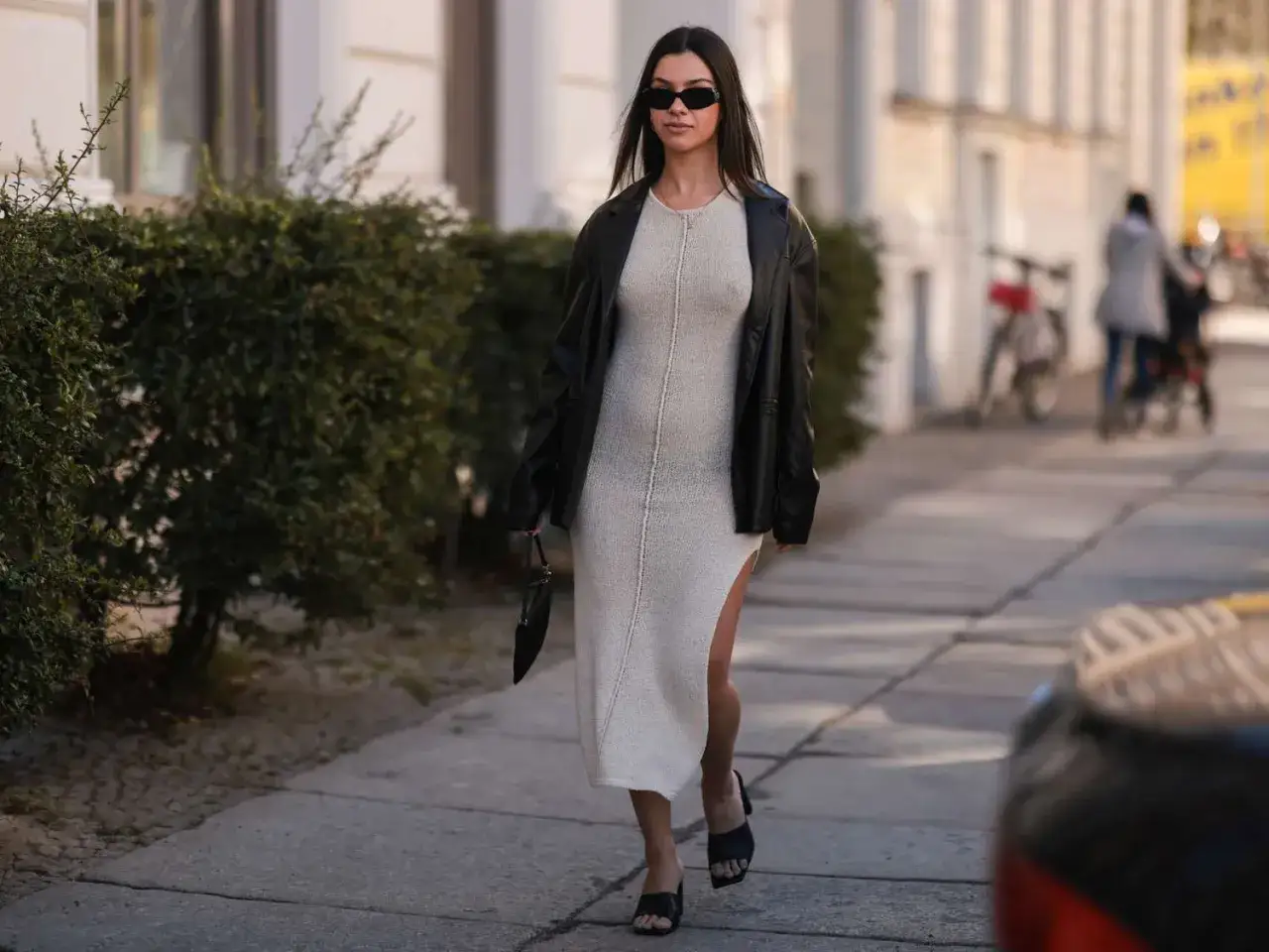 Frau tr&auml;gt ein helles Strickkleid mit Schlitz und schwarze Lederjacke. Perfekte Antwort auf die Frage: welche Jacke zu langem Kleid.