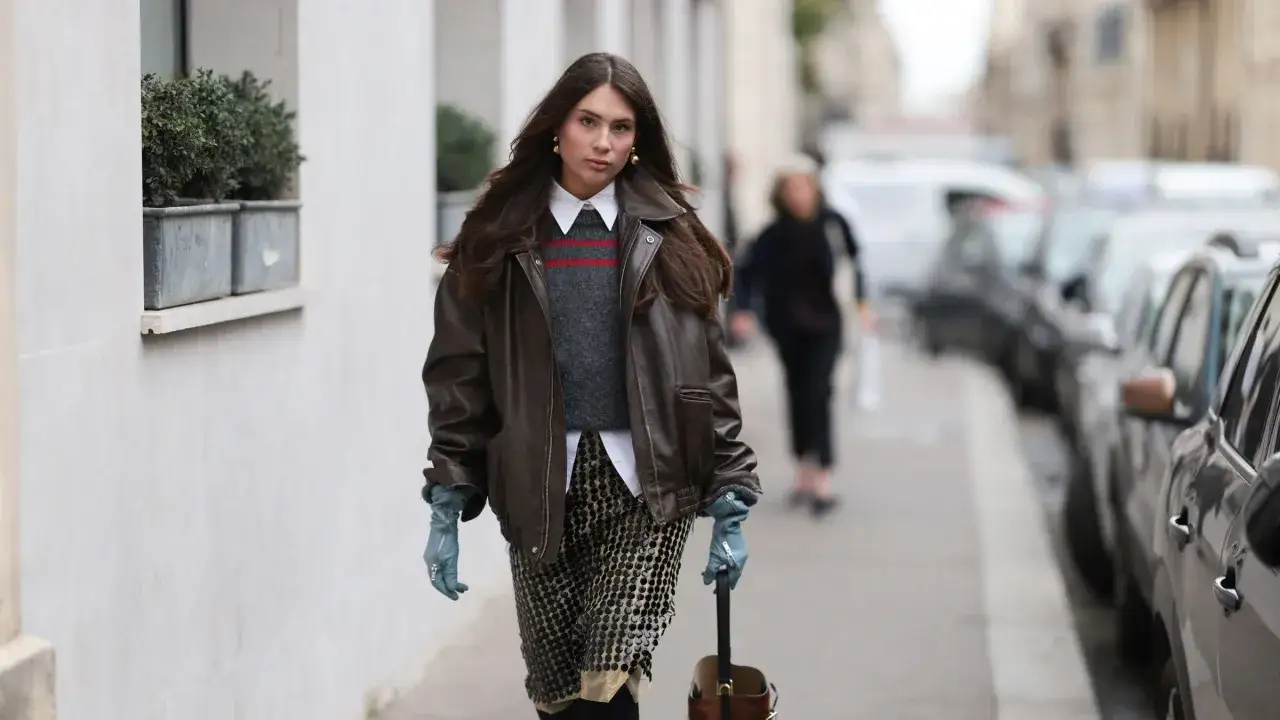 Frau im l&auml;ssigen layering look mit Lederjacke, Strickweste, Hemd und Paillettenrock.