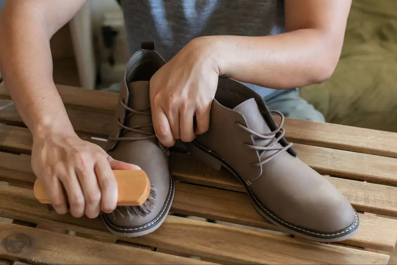 H&auml;nde b&uuml;rsten braune Lederstiefel, um sie sauber zu machen.