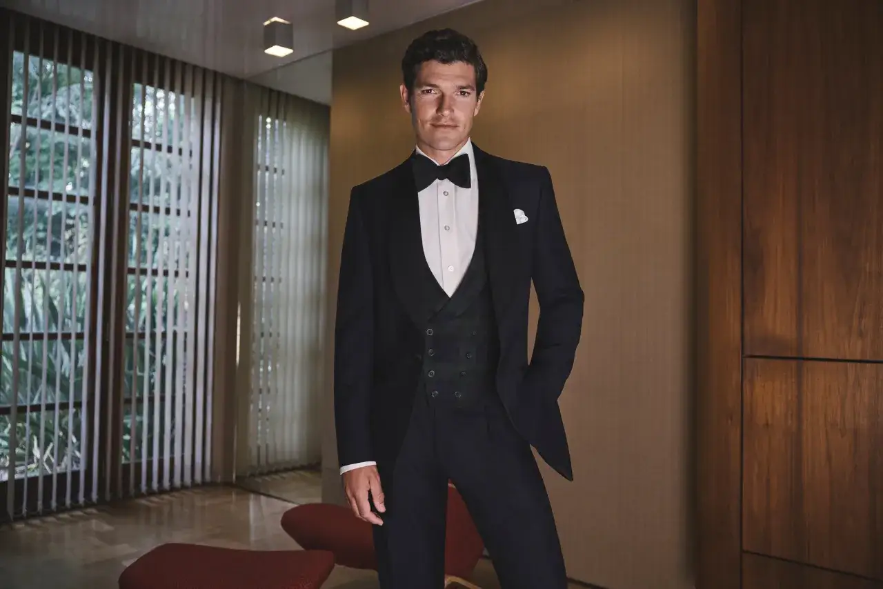 Eleganter Mann im Smoking, bereit für eine black tie party. Er trägt eine Weste mit Karomuster und eine weiße Hemdbrosche.