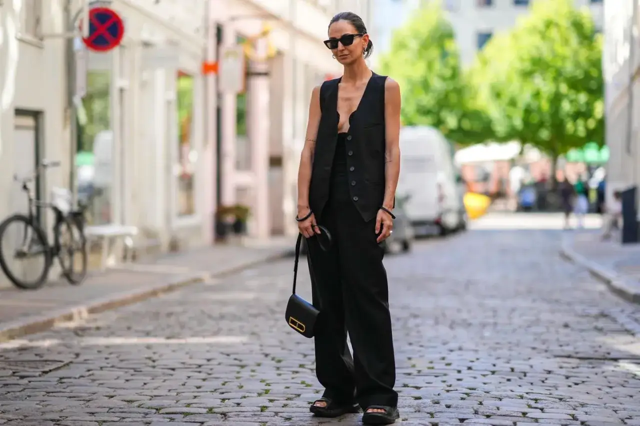 Schwarze Hose kombinieren hochzeit: Eleganter Look mit Weste und Tasche auf Kopfsteinpflaster.