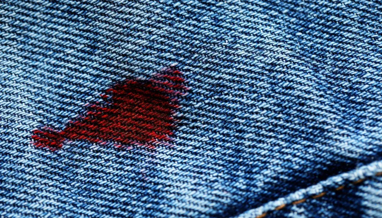 Ein roter Fleck auf blauer Jeans. Ein kleiner Unfall, der zeigt, wie man blut aus jeans entfernen kann.