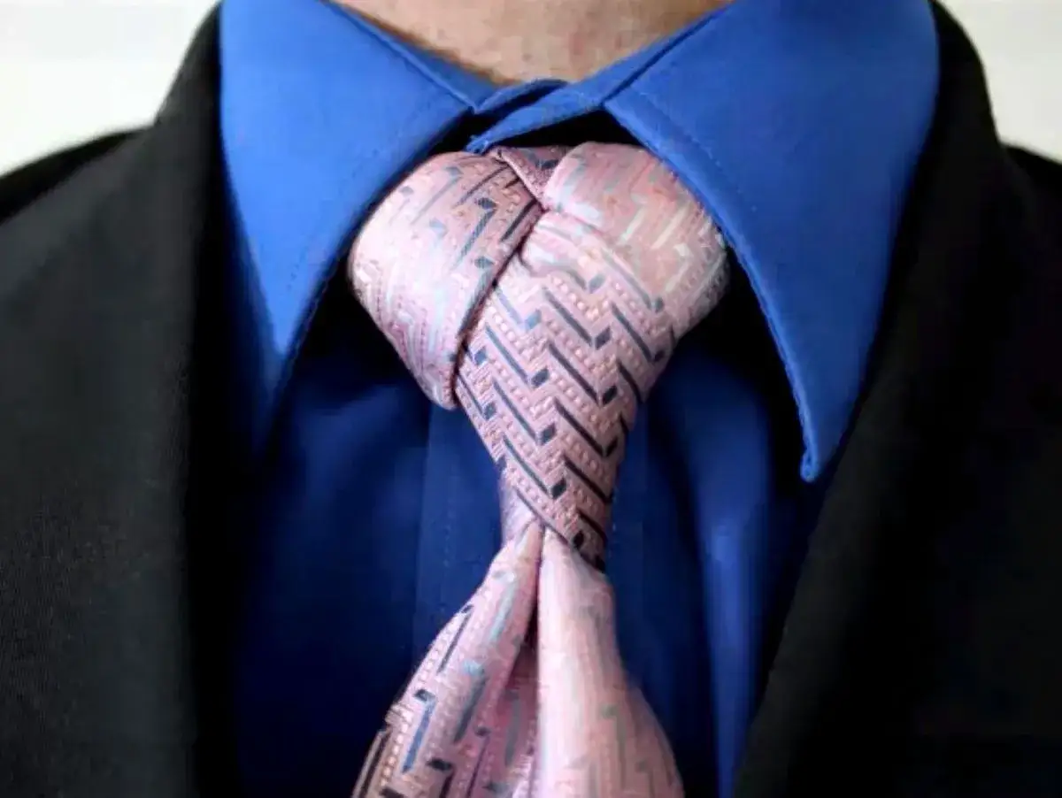 Ein Mann tr&auml;gt einen blauen Hemdkragen, einen schwarzen Anzug und eine Krawatte mit einem komplexen Muster. Verschiedene krawattenknoten arten k&ouml;nnen so elegant aussehen.