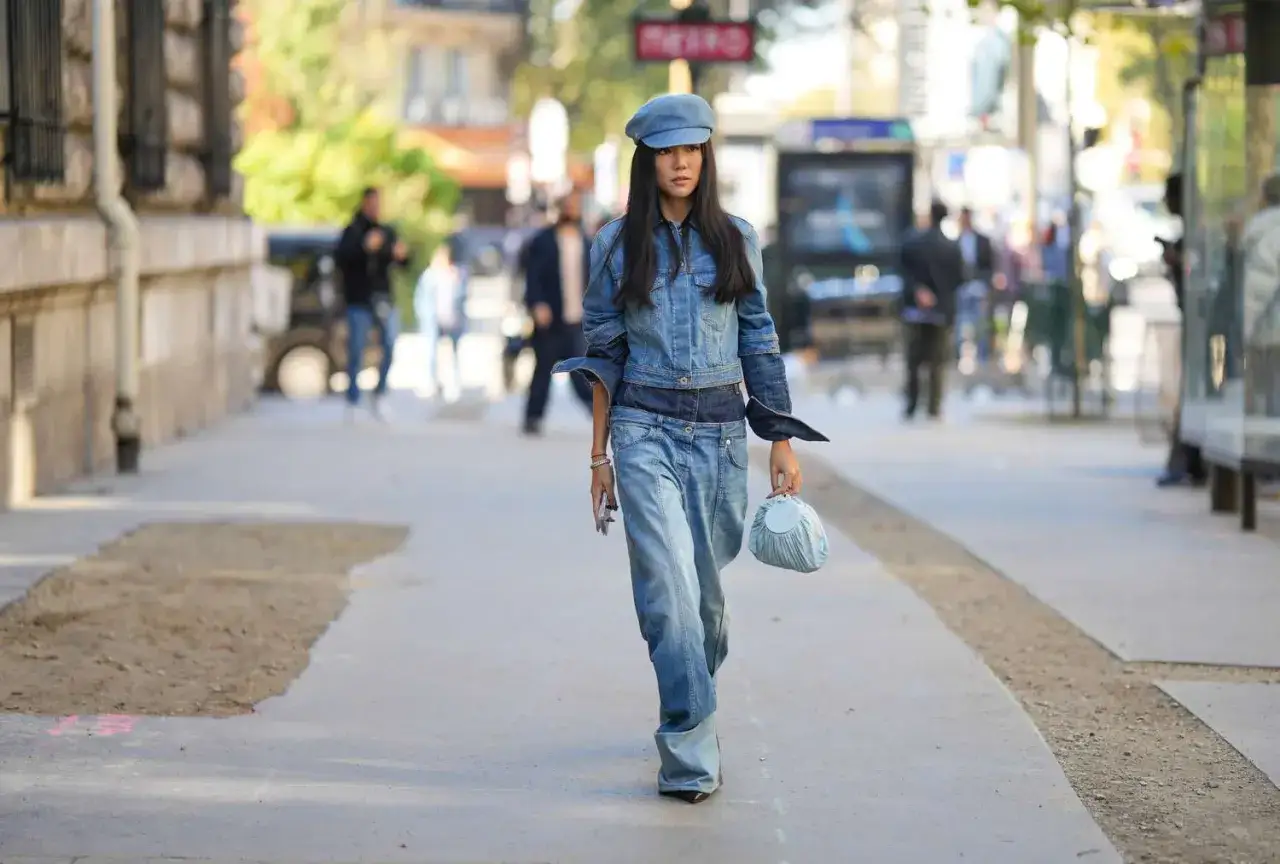 Frau in Jeansjacke und weiten Jeans, die fragt: welche hose zu jeansjacke? Sie trägt eine blaue Schirmmütze und eine kleine blaue Tasche.